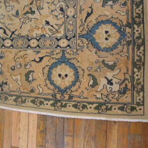 Beige rug with dense blue and green floral borders rests on warm plank hardwood flooring.