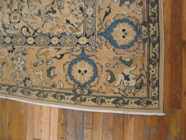 Beige rug with dense blue and green floral borders rests on warm plank hardwood flooring.