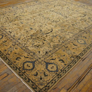 Gold rug with detailed blue and black traditional motifs covering aged, wide plank hardwood floors.