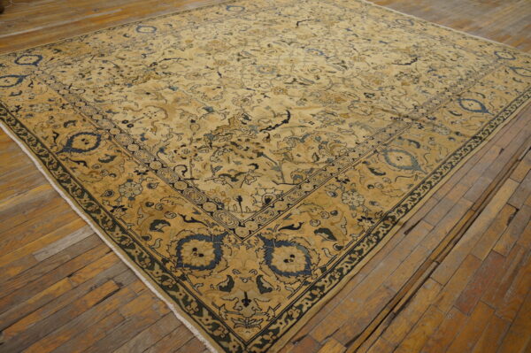 Gold rug with detailed blue and black traditional motifs covering aged, wide plank hardwood floors.