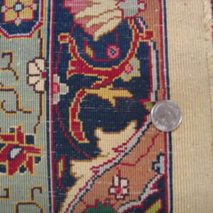 Detail of a tight-weave border pattern in navy, red, and sage green, with a silver coin providing scale.