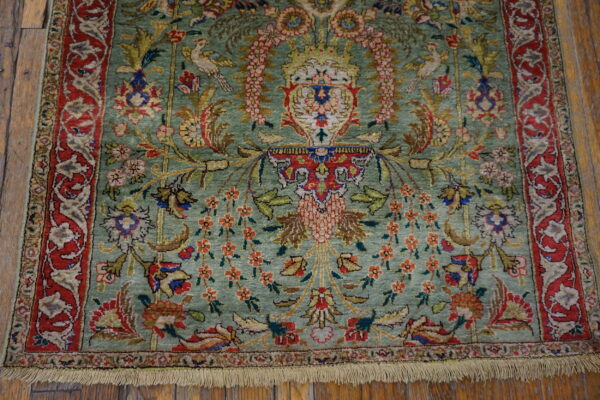 Rare green color fine luxurious silk pile antique persian tabriz islamic prayer design rug 2 Textured green rug with red borders and intricate floral and avian patterns rests on rustic wood flooring.