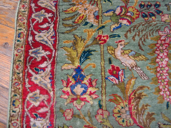 Rare green color fine luxurious silk pile antique persian tabriz islamic prayer design rug 4 Close-up shows a multicolored traditional rug, green field, red border, and floral and bird pattern on wood.