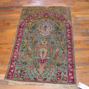 Ornate green and red rug with a central arch motif lying on distressed orange wooden floorboards.
