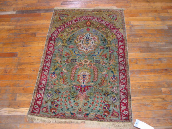Rare green color fine luxurious silk pile antique persian tabriz islamic prayer design rug 7 Ornate green and red rug with a central arch motif lying on distressed orange wooden floorboards.