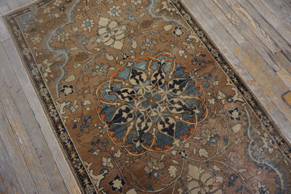 Brown rug featuring complex blue, cream, and orange floral patterns resting on weathered wood flooring.