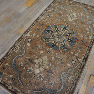 Low-pile rug in earthy brown, blue, and cream with an ornate medallion on distressed wood flooring.