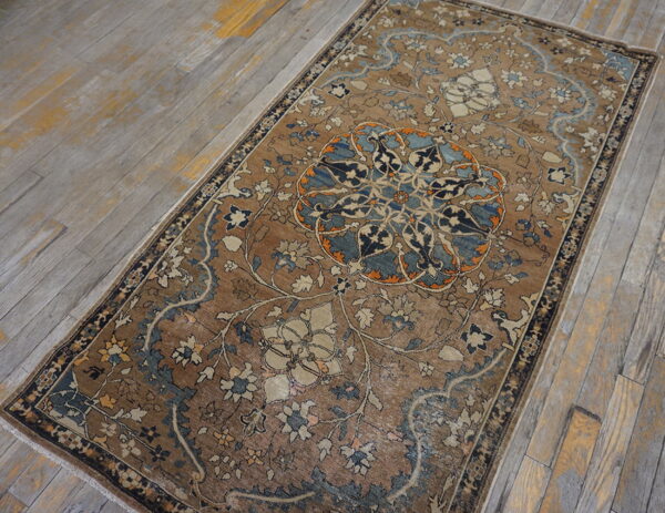 Low-pile rug in earthy brown, blue, and cream with an ornate medallion on distressed wood flooring.