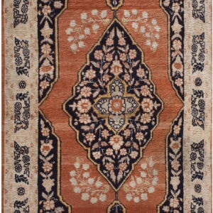 Low-pile rug with a navy floral medallion on a terracotta field and a densely patterned beige border.