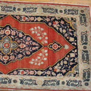 Traditional low-pile rug featuring a red field, navy floral medallion, and beige borders on wood flooring.