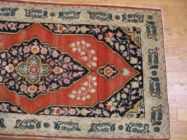 Traditional low-pile rug featuring a red field, navy floral medallion, and beige borders on wood flooring.
