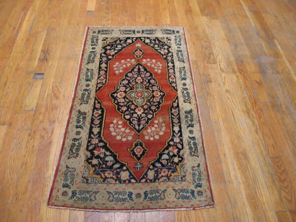 Ornate rust red and navy medallion rug with sage borders lying on distressed hardwood floors.
