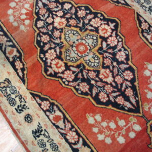 Rust red, navy, and cream traditional rug with floral medallions lying on wood planks.