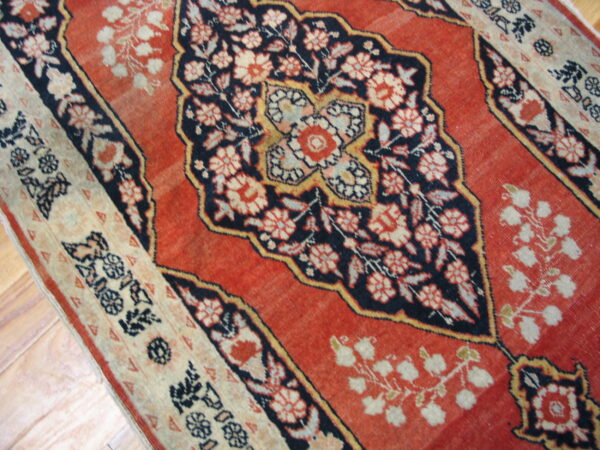 Rust red, navy, and cream traditional rug with floral medallions lying on wood planks.