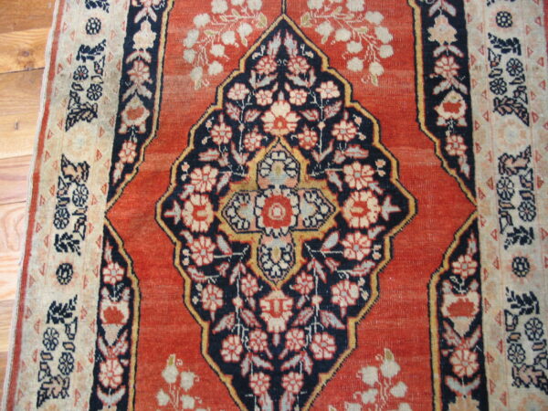 Ornate red rug with a dark blue and beige floral medallion on light hardwood flooring.