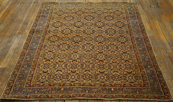 Traditional low pile rug in ochre, rust, and blue geometric floral patterns on distressed wood flooring.