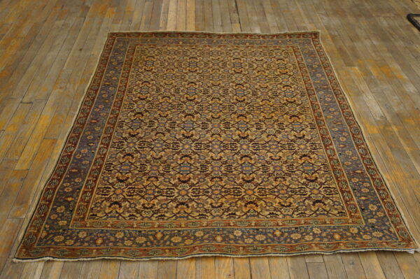A low-pile rug featuring complex repeating patterns in tan, blue, and rust rests on distressed wooden floors.