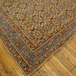 Low pile traditional rug corner with detailed floral design in tan, blue, and rust colors on wood flooring.