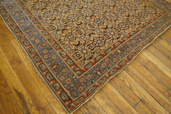 Low pile traditional rug corner with detailed floral design in tan, blue, and rust colors on wood flooring.