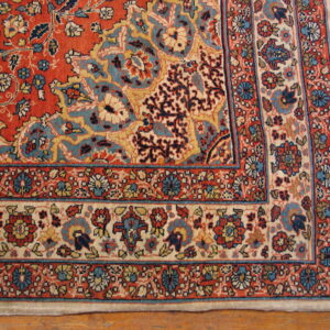 Intricate floral rug featuring a red field, blue, and cream borders, resting on hardwood flooring.