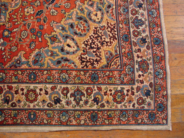 Intricate floral rug featuring a red field, blue, and cream borders, resting on hardwood flooring.