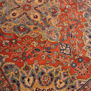 Intricate floral rug design with a deep red field accented by teal blue, cream, and gold scrollwork.