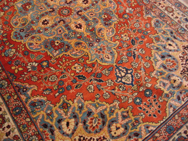 Intricate floral rug design with a deep red field accented by teal blue, cream, and gold scrollwork.