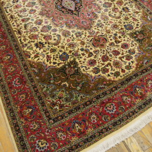 Cream field rug featuring intricate traditional floral designs, deep red borders, and visible white fringe on wood flooring.