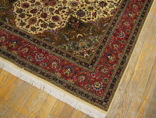 Ornate traditional rug with cream and red floral patterns, white fringe, lying on distressed wood planks.