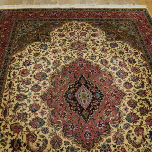 Cream and red ornate medallion rug with floral patterns covering distressed yellow wood floorboards.