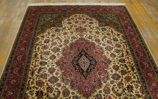 Cream and red ornate medallion rug with floral patterns covering distressed yellow wood floorboards.