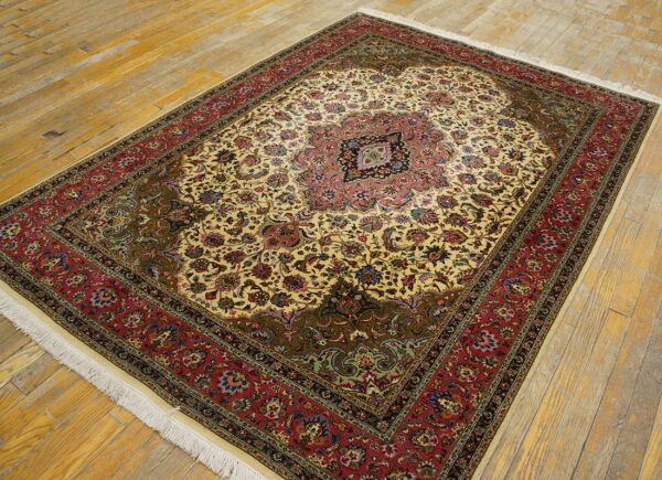 Ornate traditional rug featuring an ivory field, pink medallion, and red border on yellow wooden flooring.