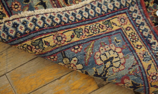 Intricate blue, gold, and red patterned rug edge rolled over distressed yellow wood flooring.