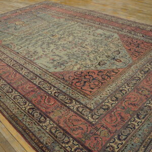 Ornate traditional rug with a light blue central field and complex dusty rose borders on plank flooring.