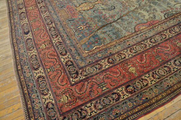 Ornate low-pile rug featuring a blue field with tree pattern and wide red floral borders on hardwood.
