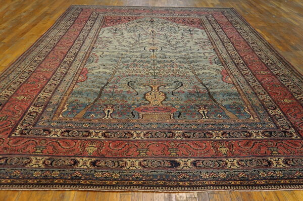 Large traditional rug with a central blue tree of life pattern and wide coral and navy floral borders on a wood floor.