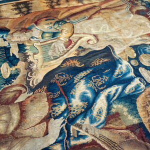 Intricate pictorial tapestry featuring figures and nature motifs in muted blues, beige, and brown tones.