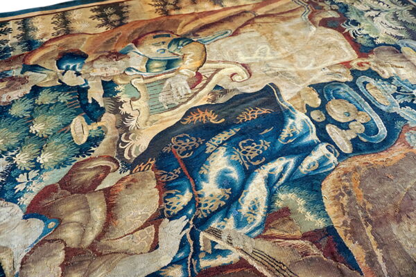 Intricate pictorial tapestry featuring figures and nature motifs in muted blues, beige, and brown tones.