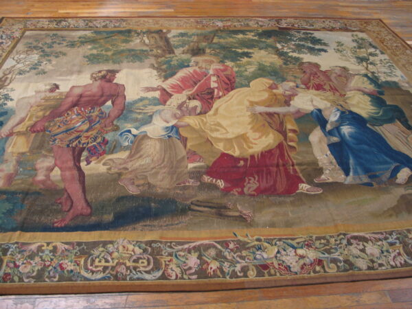 Low-pile rug depicting a scenic classical tapestry design with figures in red, gold, and blue robes on wood flooring.