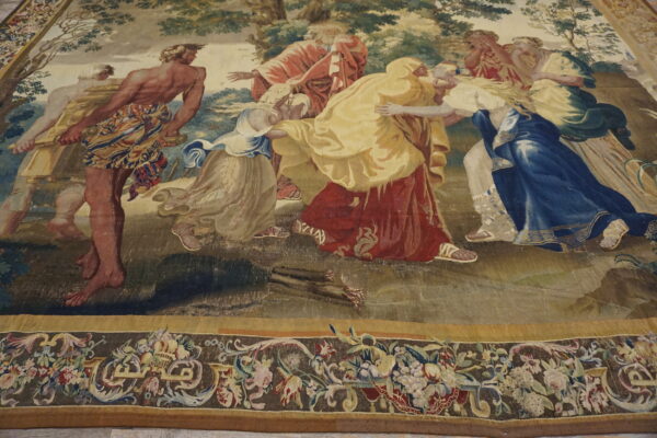 Figurative tapestry-style rug depicts figures in red and blue robes, framed by a detailed floral border on the floor.