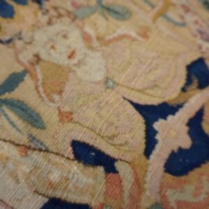 Detailed close-up of a low-pile rug featuring figural and floral patterns in blue, pink, and pale yellow.