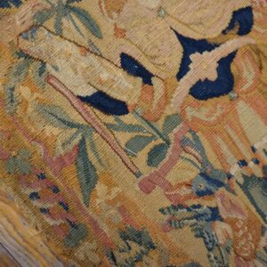 Detailed flatweave rug fragment with pictorial designs in muted gold, blue, pink, and green on wood planks.