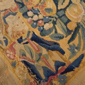 Damaged low-pile rug featuring a densely woven floral pattern in navy, gold, green, and red.