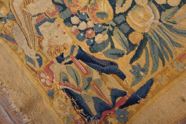 Damaged low-pile rug featuring a densely woven floral pattern in navy, gold, green, and red.