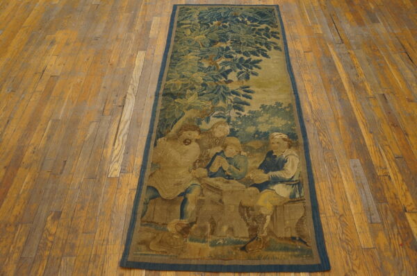 A long, low-pile rug featuring a muted blue and tan figurative scene is laid upon rustic wood planks.