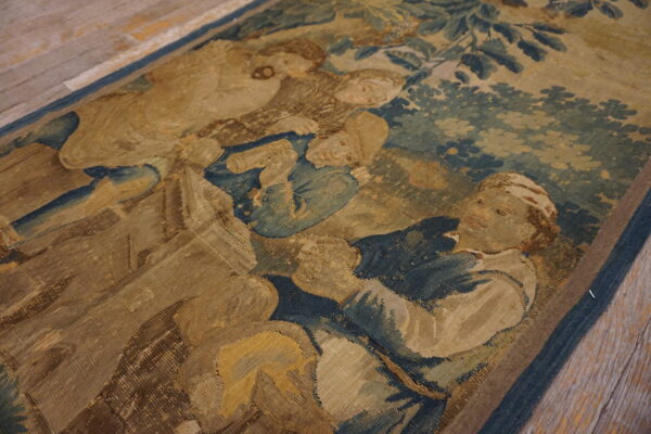 Woven tapestry rug in muted tan, blue, and brown depicting a historical figurative scene on wood floor.
