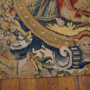Muted blue, gold, and red woven tapestry fragment featuring figural details rests on cracked wood floorboards.