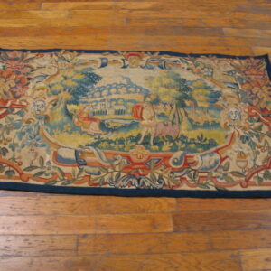 Rectangular tapestry-style rug with a detailed scenic blue and gold medallion lies on plank hardwood flooring.