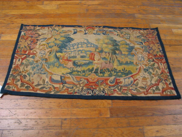 Rectangular tapestry-style rug with a detailed scenic blue and gold medallion lies on plank hardwood flooring.