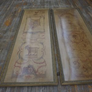Two framed, elongated beige textiles with classical red and blue patterns rest on worn gray wood flooring.